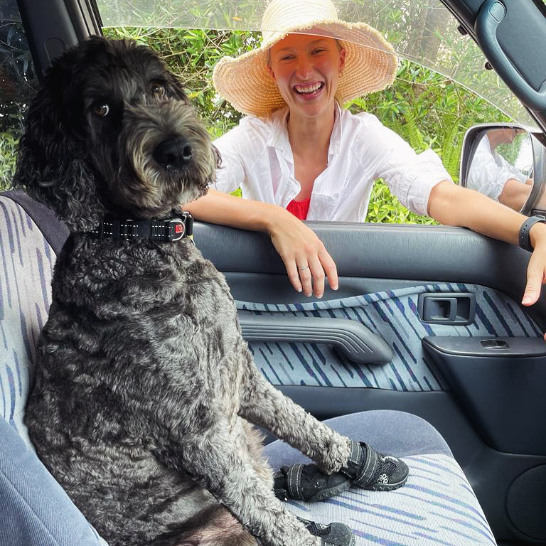 Tess Victory standing with a sunhat on looking at her dog sitting in the front seat of a car